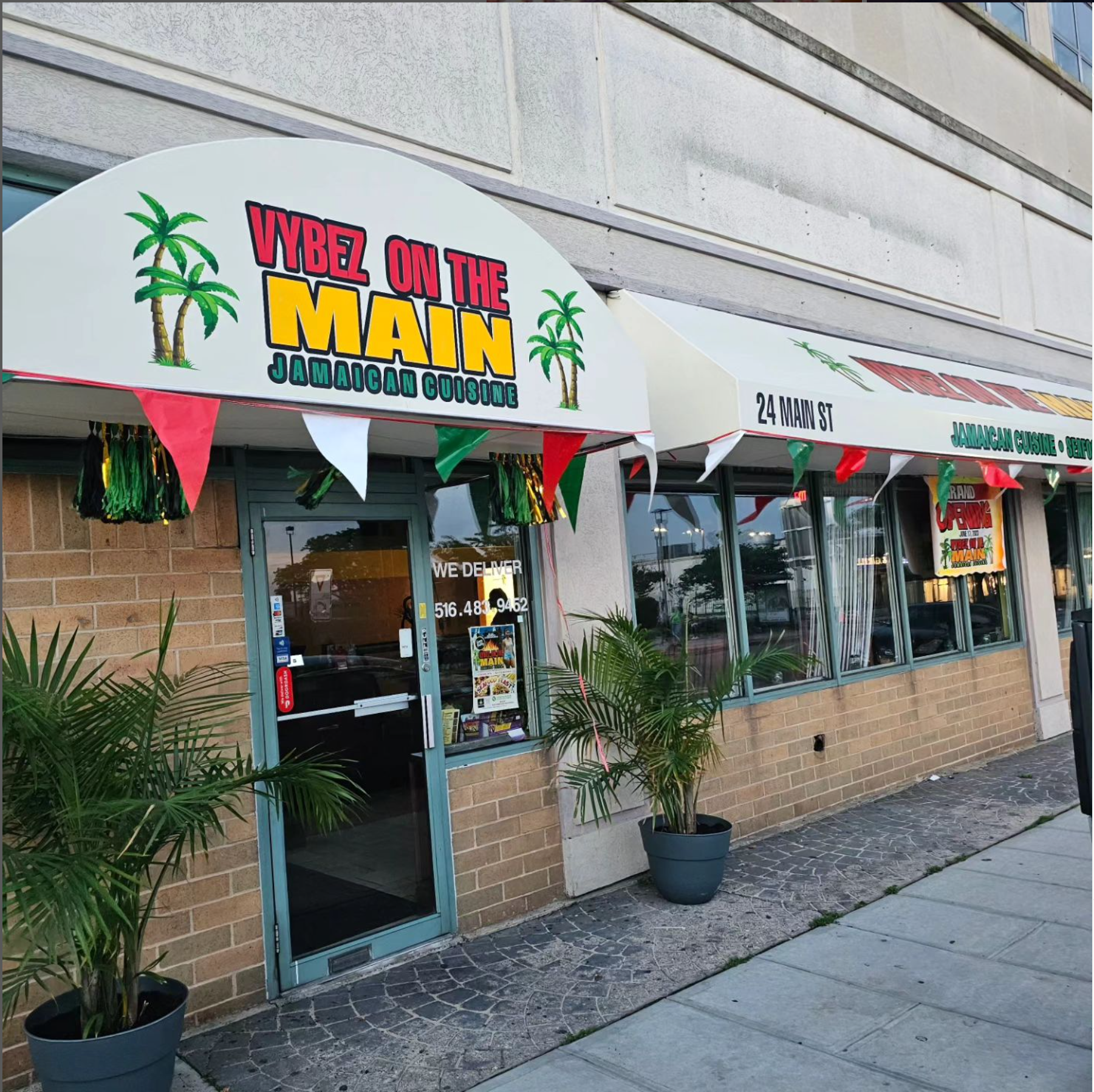 Photo of restaurant storefront with a white awning that displays red yellow and green Vybez On The Main logo