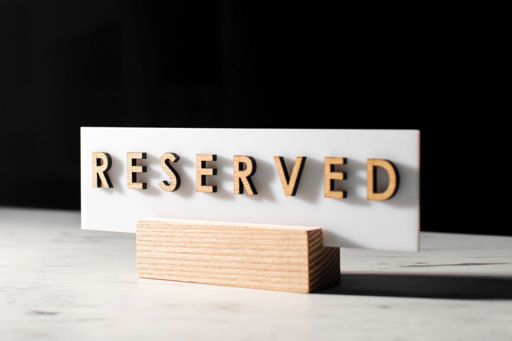 Capital woodcut letters spell the word 'RESERVED' on a white card mounted above a rectangular wooden block